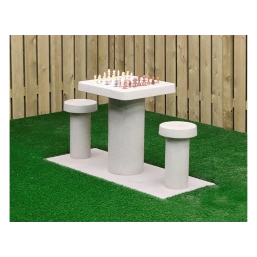 Skakbord i beton til to personer med skakbrikkerne placeret på og stående i en have med grønt underlag ved siden af et stakit