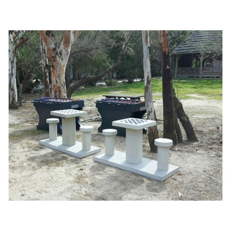 To lyse skakborde i beton placeret ved to bordfodboldborde i en skov med en flot træhytte i baggrunden