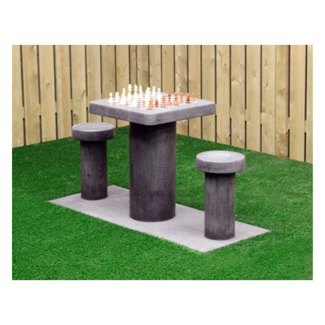 Skakbord i grå beton med plads til to personer placeret i hjørnet af en have med grønt græs og et træfarvet stakit