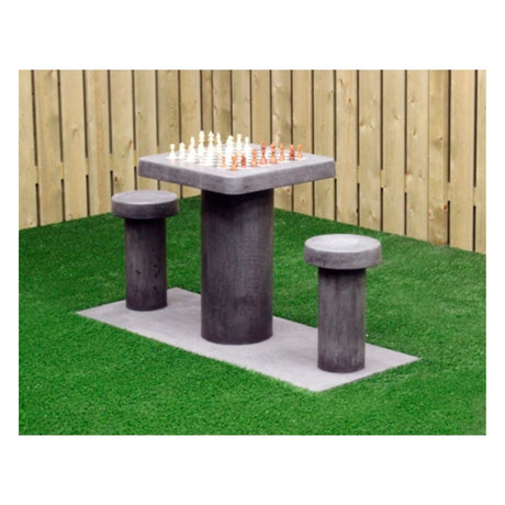 Skakbord i grå beton med plads til to personer placeret i hjørnet af en have med grønt græs og et træfarvet stakit