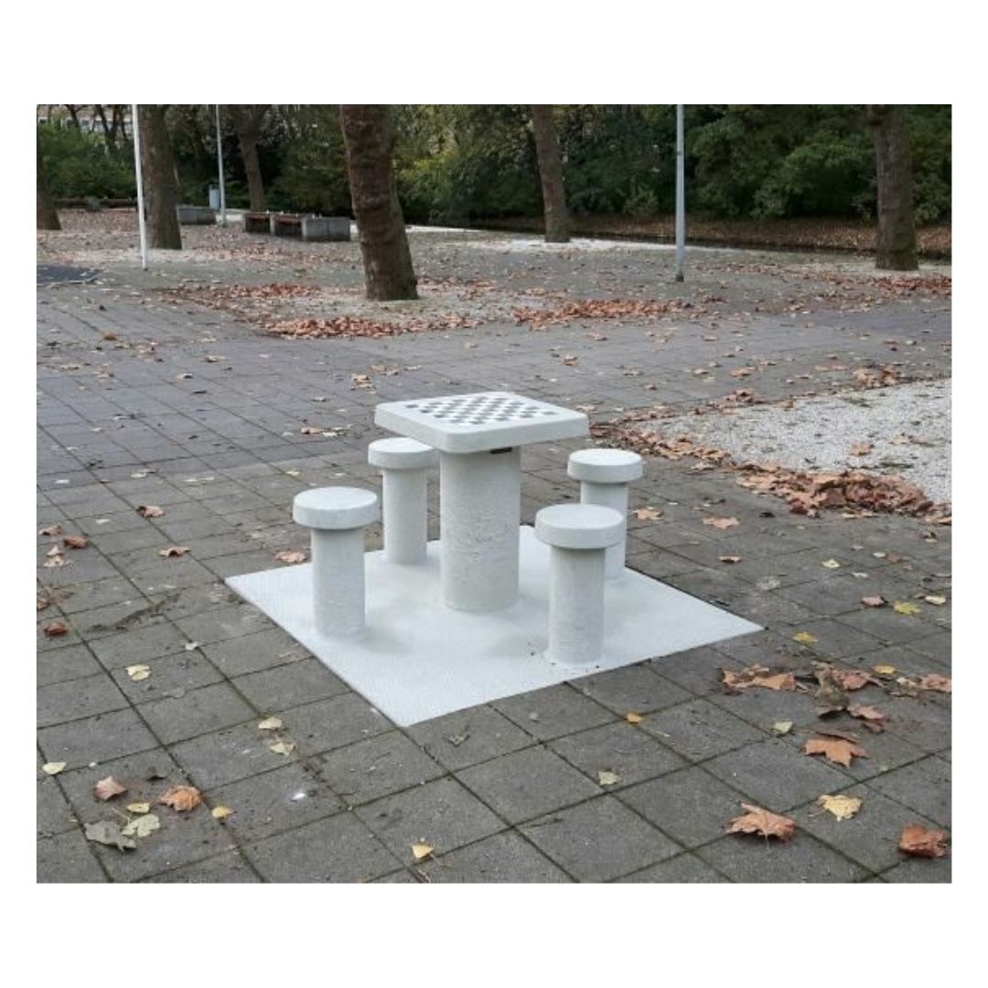 Skakbord i beton placeret på et en åben plads omgivet af fliser og blade der er faldet i træerne i løbet af efteråret