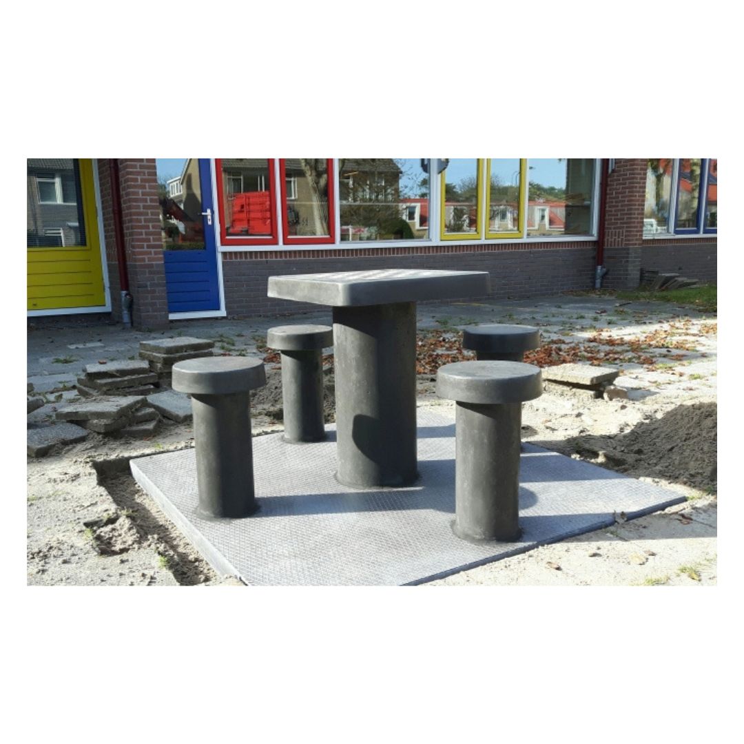 Skakbord i beton med plads til fire personer placeret ude foran en skole med farvede vinduer