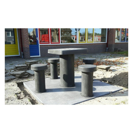 Skakbord i beton med plads til fire personer placeret ude foran en skole med farvede vinduer