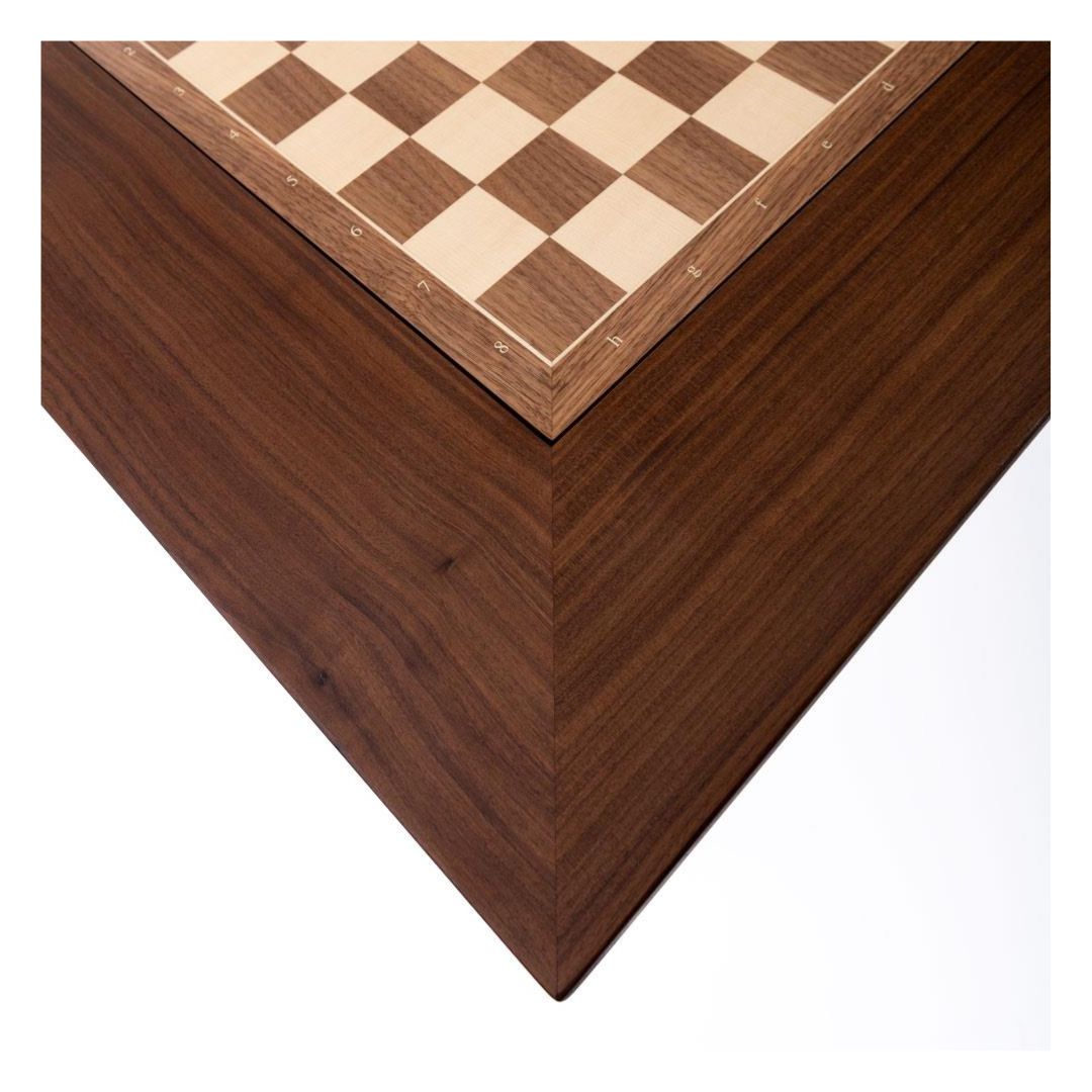 Hjørnet af et skakbord med skakbræt begge i valnød sat i. Bordet er en smule mørkere end skakbrættet