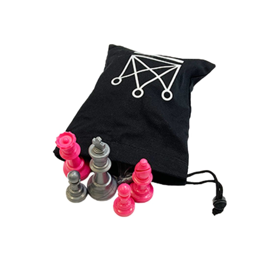 Skakbrikker i plastik i farverne sølv og pink stående foran en sort brikpose i stærk bomuld med en krone påtrykt