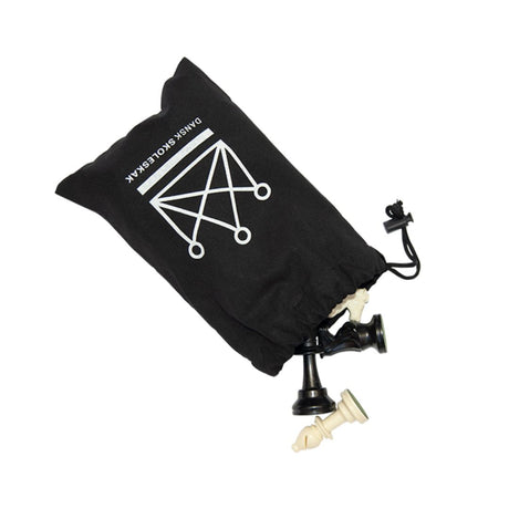 En sort stofpose med snoretræk og hvidt logo fra Dansk Skoleskak, hvorfra flere sorte og hvide skakbrikker i plastik stikker ud mod en hvid baggrund.